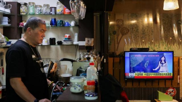 A person stands in a cafe as a news broadcast shows China announcing new military drills around Taiwan, in Keelung, Taiwan, May 23, 2024.